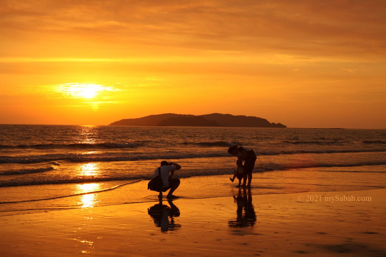 A family with child at Tanjung Aru Beach during sunset