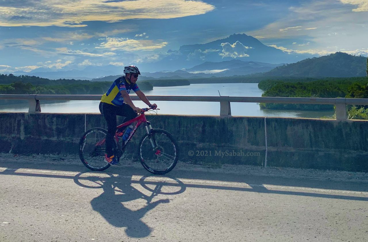 Cycling on Mengkabong River Bridge with the view of Mount Kinabalu